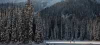 Two people in the distance walking through the snow, surrounded by trees and mountains