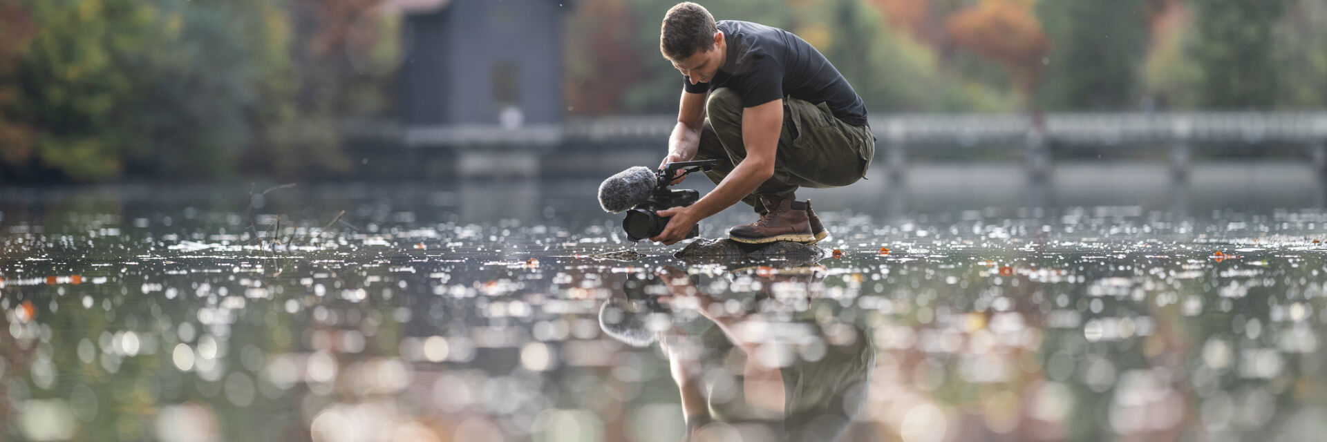 Young man photographing with camera over water in lake